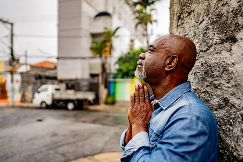 A man praying with folded hands, reflecting on his faith and searching for answers to the question: is it okay to doubt.