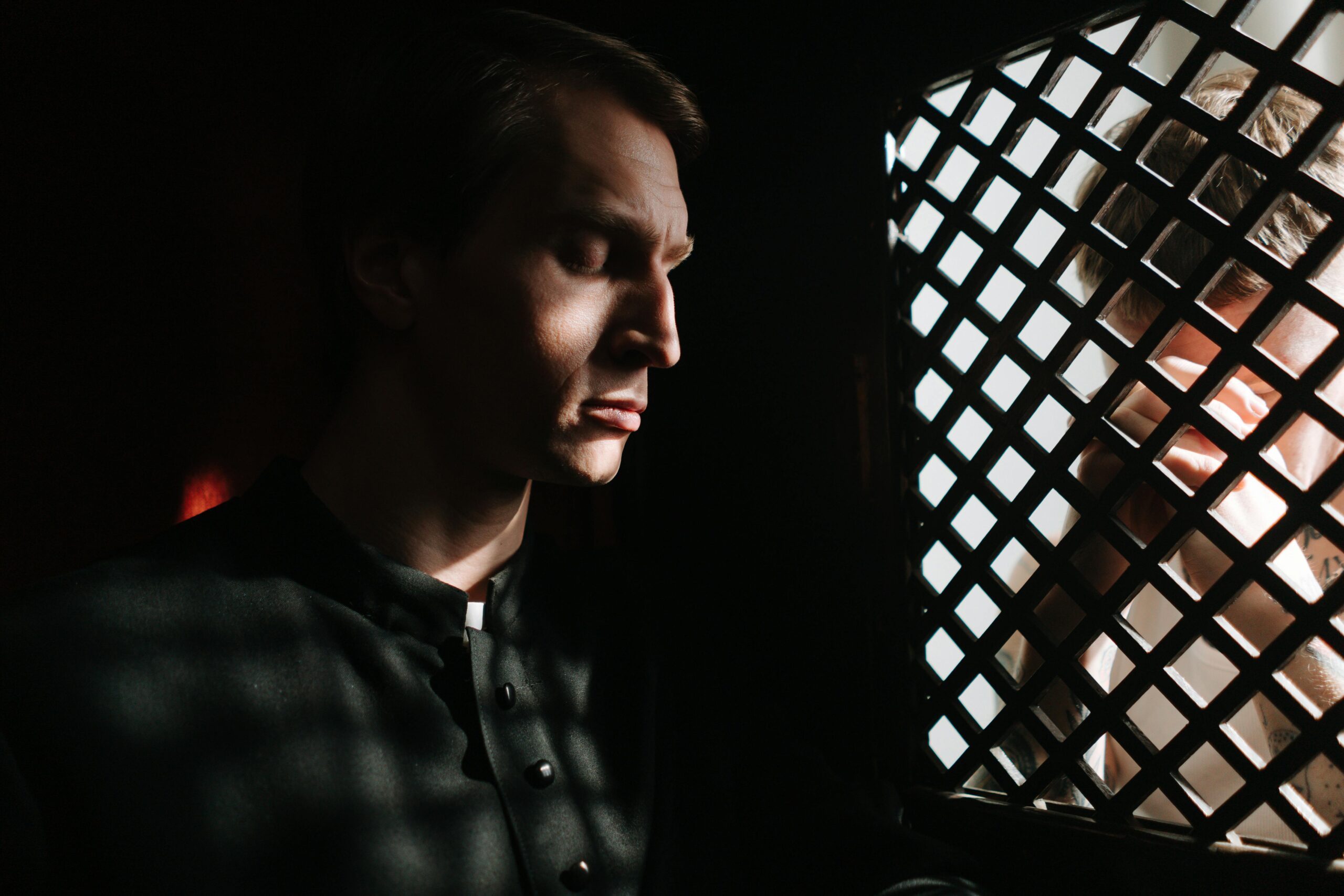 A man in a confessional talking to a priest, representing the sacrament of reconciliation and the spiritual path of forgiveness.