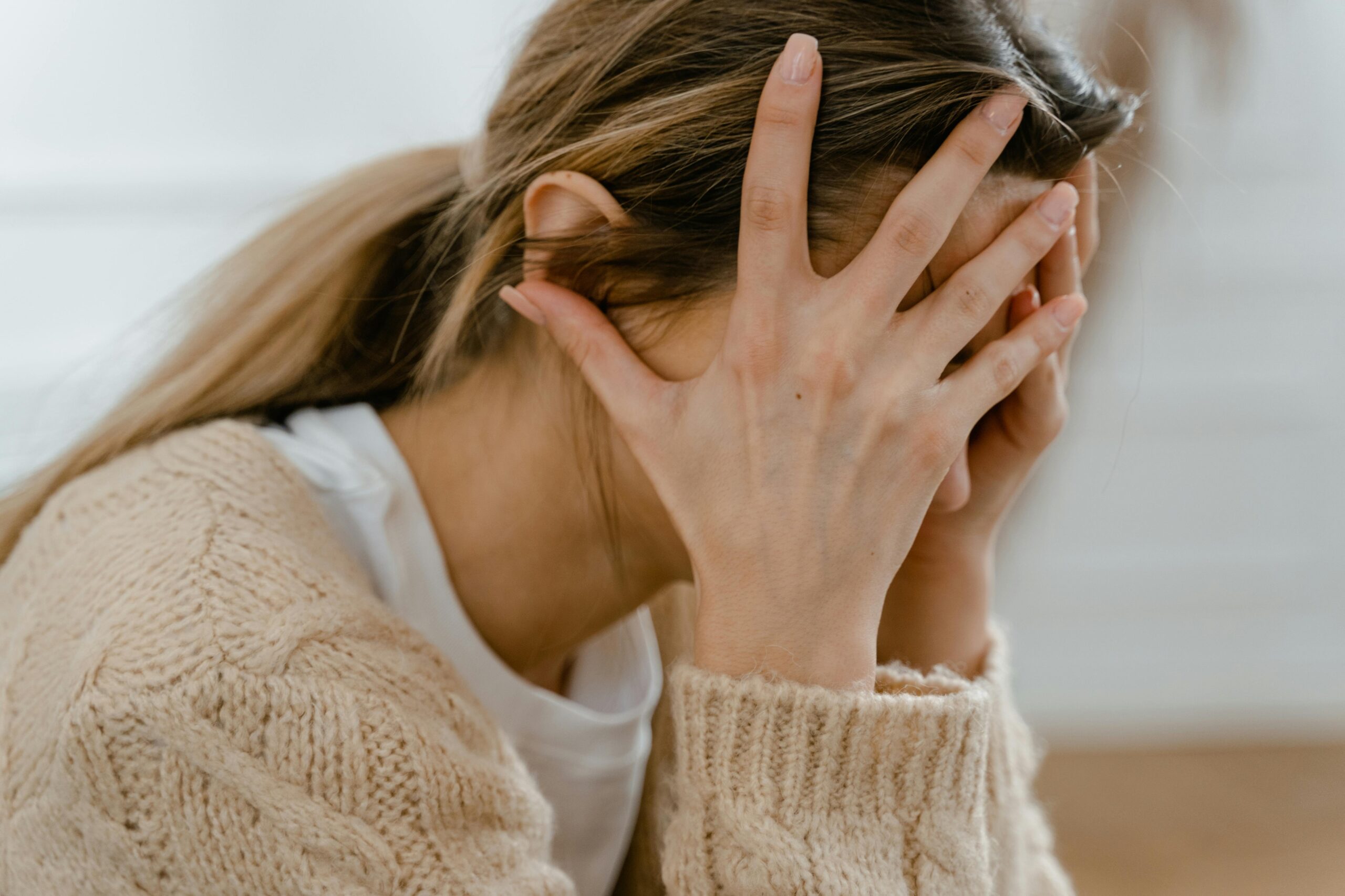 A woman holding her head in her hands, feeling overwhelmed and looking for ways of letting go of worry and anxiety through faith.