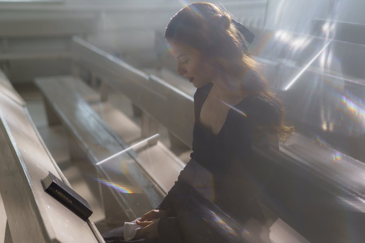 A young woman sitting peacefully in a church pew with soft light streaming in.